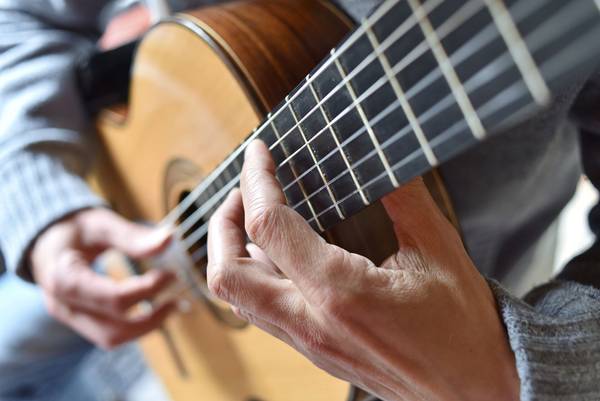 Nauaufnahme einer Person, die Gitarre spielt. Man sieht die Hände und die Gitarrenseiten.